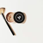 Flat lay of a makeup brush and scrub container on a white surface, perfect for beauty and skincare themes.