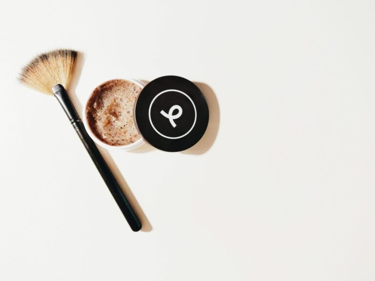 Flat lay of a makeup brush and scrub container on a white surface, perfect for beauty and skincare themes.
