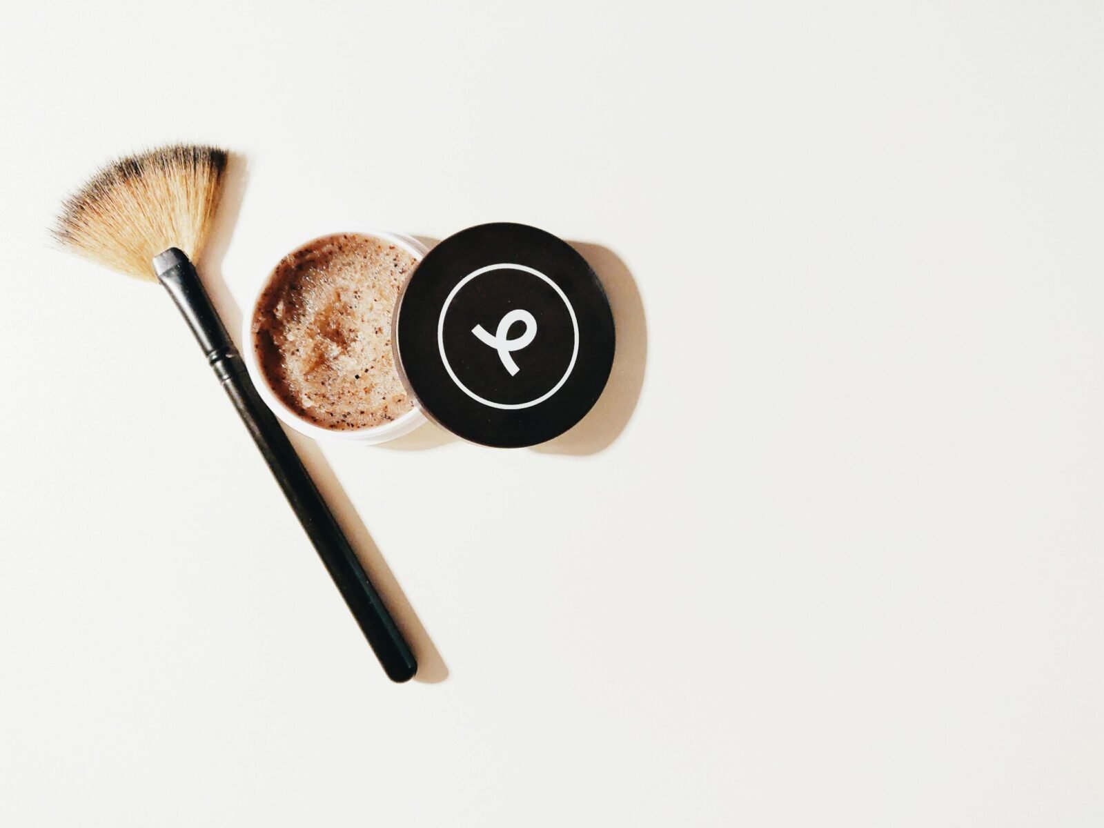 Flat lay of a makeup brush and scrub container on a white surface, perfect for beauty and skincare themes.