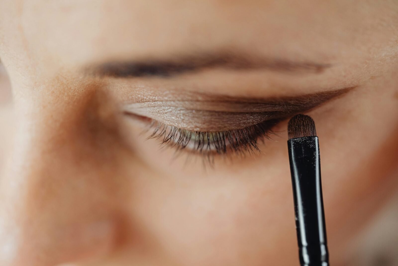Detailed close-up of an eye being carefully enhanced with eyeshadow using a makeup brush.