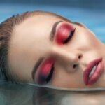 Artistic close-up of a woman with vibrant makeup submerged in water, highlighting beauty and serenity.